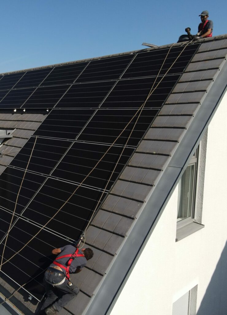PV-Anlagen auf einem Dach. 2 Montierende sind an Seilen abgesichert.