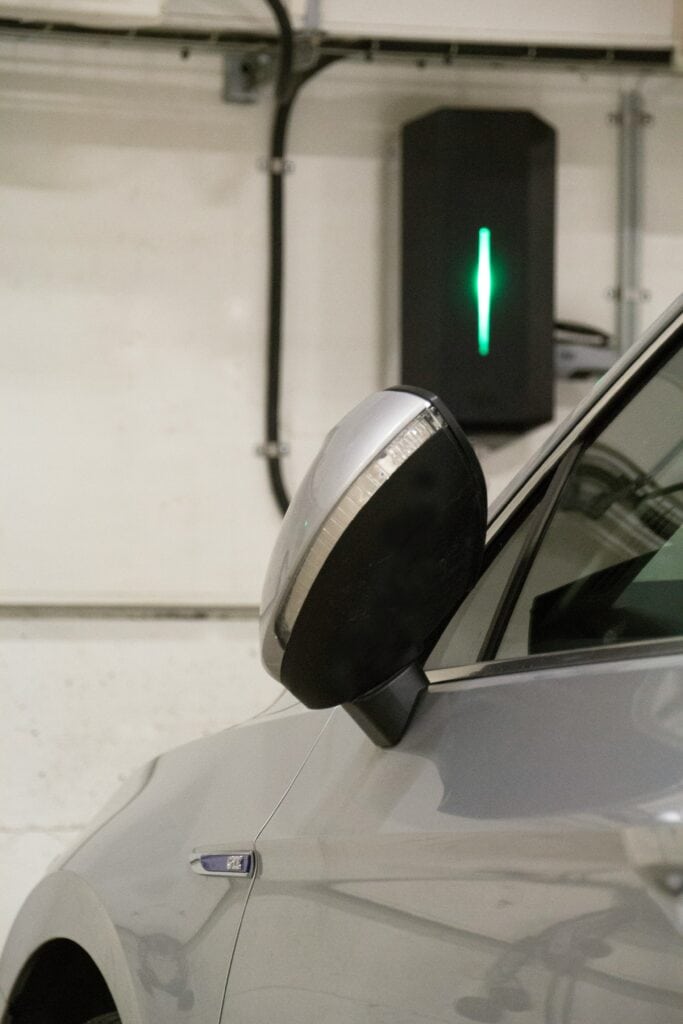 Ein eingeklappter Seitenspiegel eines Autos. Dahinter befindet sich an einer Wand eine Wallbox.