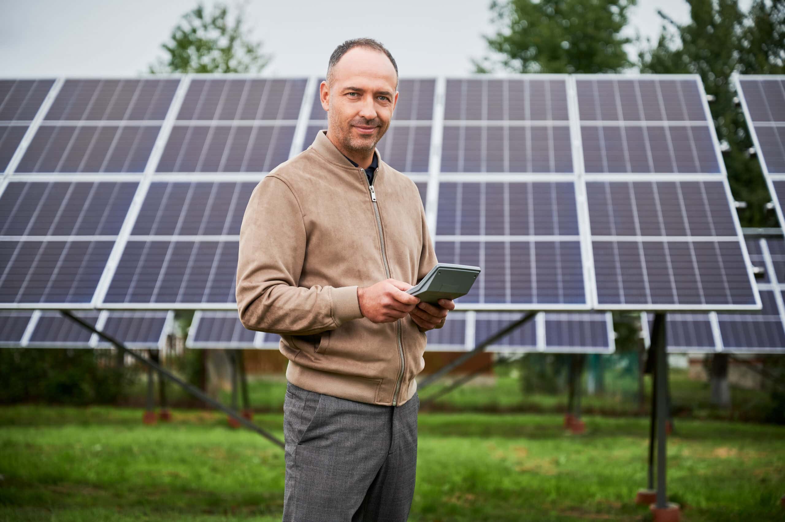 Mann mit Tablet steht vor einer Freiflächen-Photovoltaikanlage und berechnet die Wirtschaftlichkeit seiner Solarinvestition im Jahr 2025.