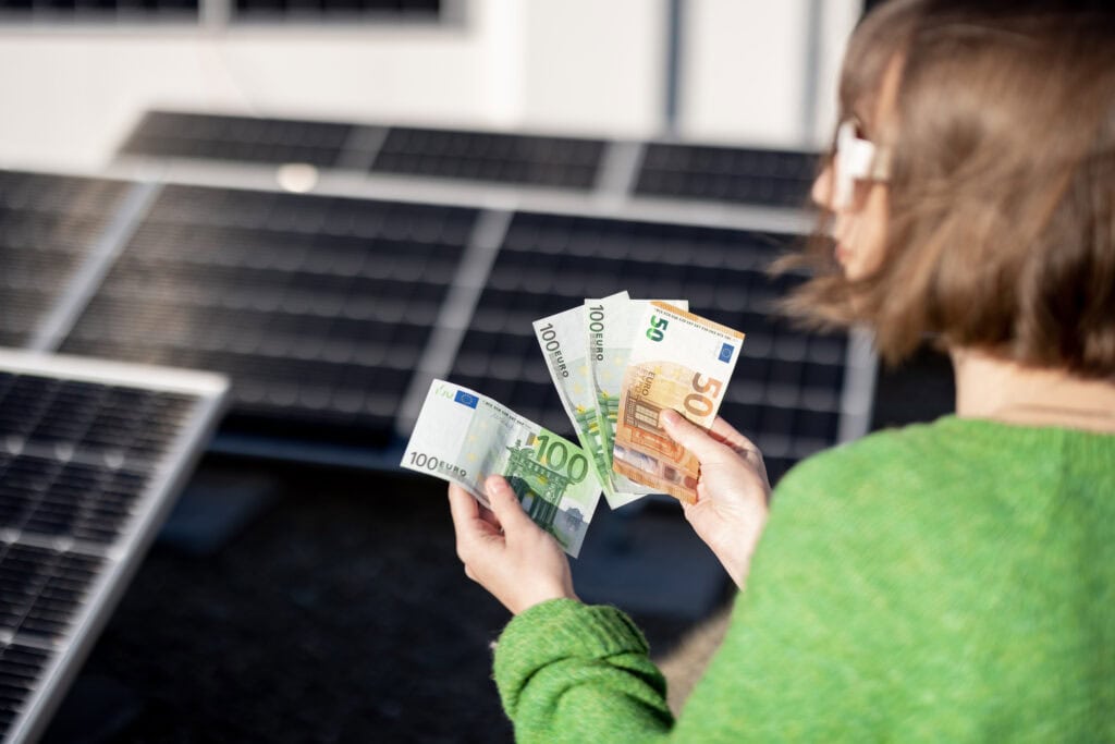 Photovoltaik lohnt sich: Frau zählt Euro-Scheine vor PV-Anlage als Symbol für Einsparungen und Wirtschaftlichkeit durch Solarstrom