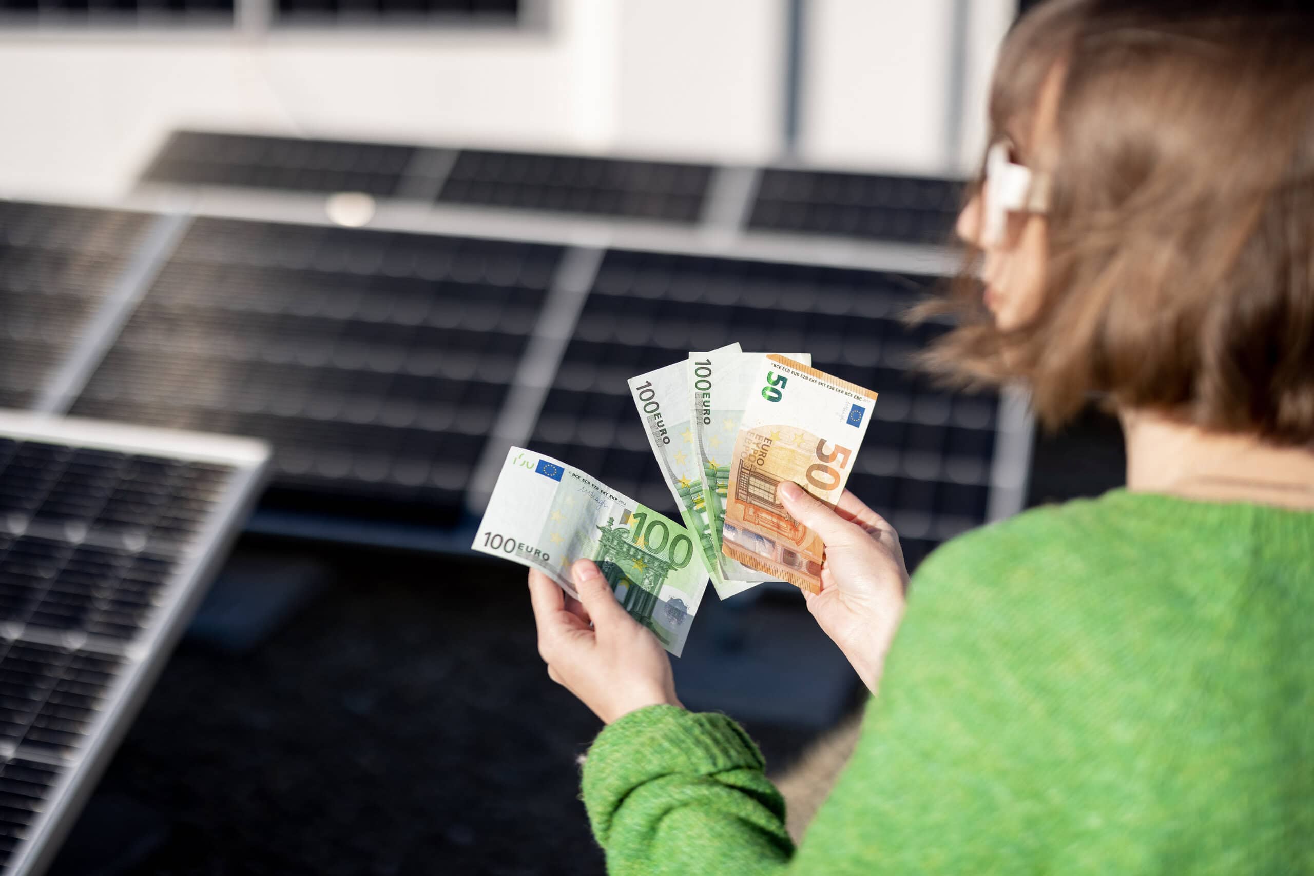 Photovoltaik lohnt sich: Frau zählt Euro-Scheine vor PV-Anlage als Symbol für Einsparungen und Wirtschaftlichkeit durch Solarstrom