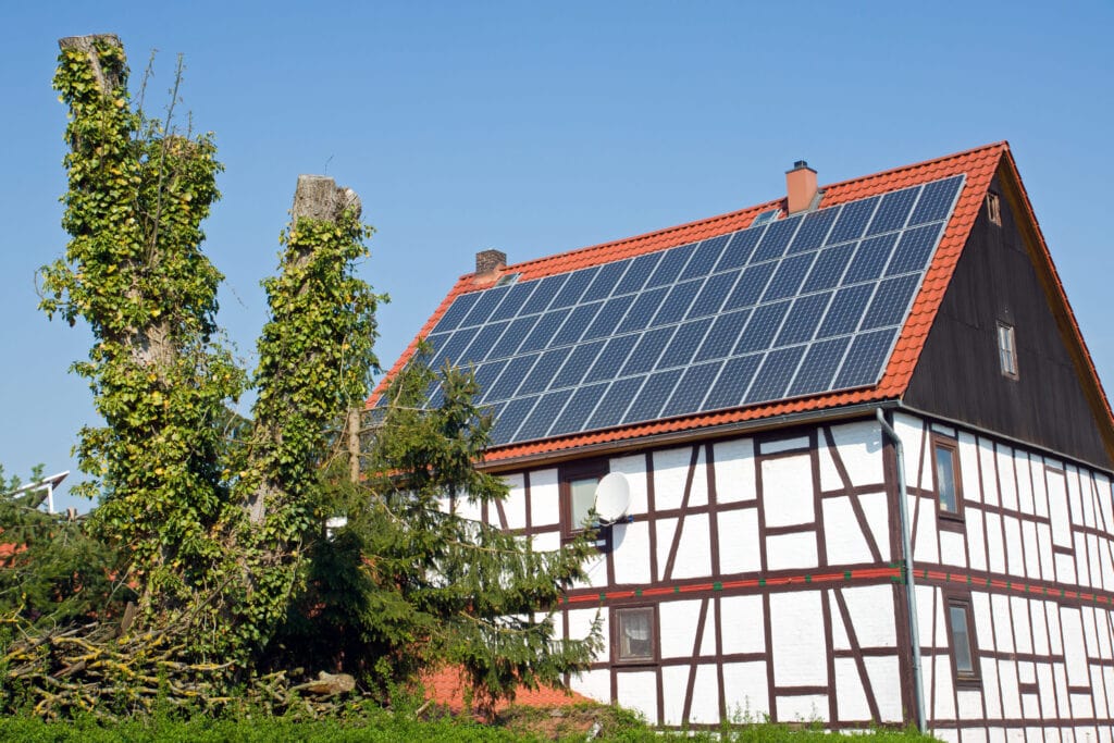 Ein traditionelles Fachwerkhaus mit einer großen Solaranlage auf dem Dach, mit der die Bewohner Photovoltaik-Strom einspeisen und selbst verbrauchen.