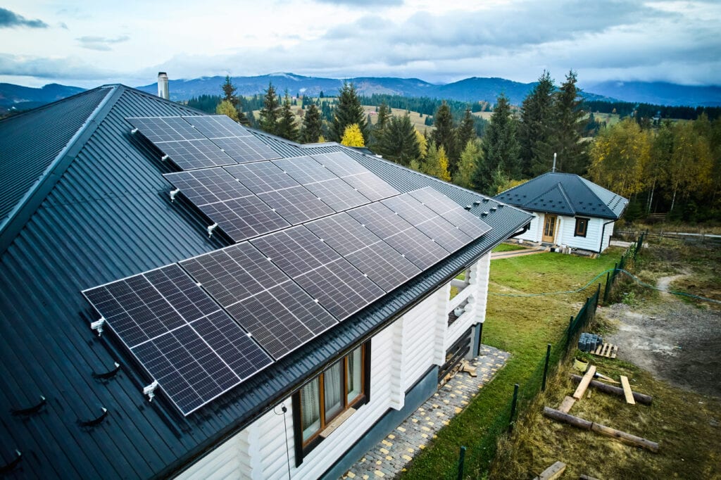 Photovoltaikanlage auf dem Schrägdach eines Einfamilienhauses aus der Vogelperspektive, mit mehreren Solarmodulen und grüner Landschaft im Hintergrund